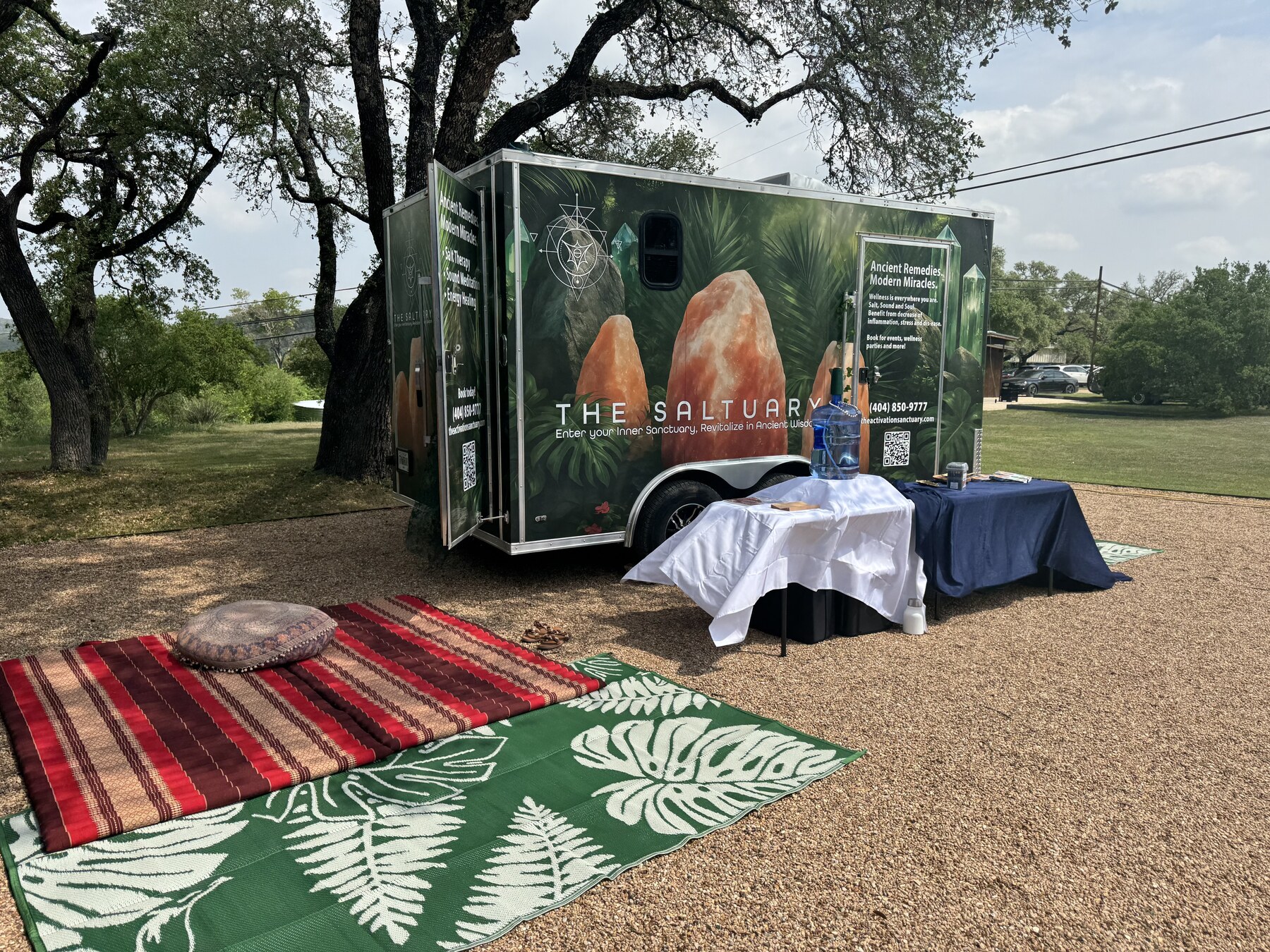 The Saltuary set up outdoors beneath trees with welcome tables, rugs, and a meditation cushion
